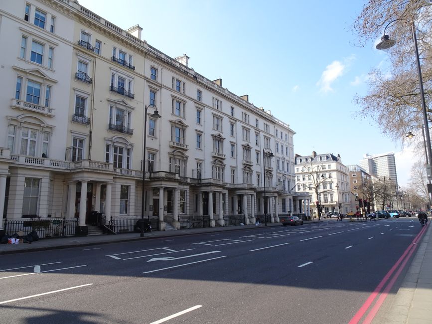 A detailed view of the exterior of a historic red brick building with ornate stone features, large arched windows, and decorative gables, located on Exhibition Road in South Kensington. The building h